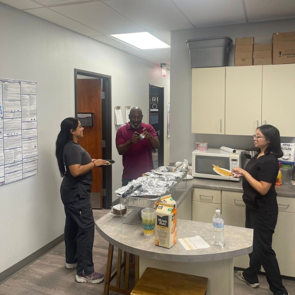 Three people in a break room are enjoying a meal
